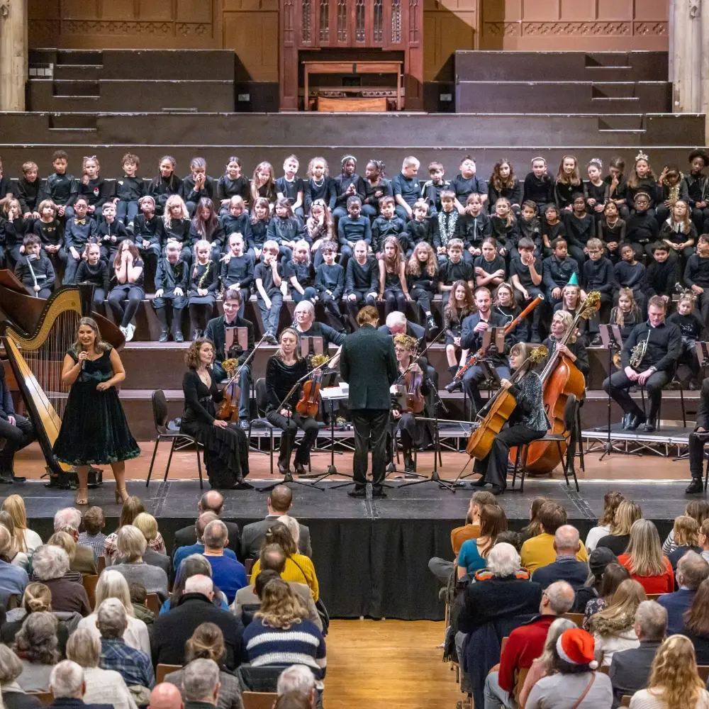 Choir and orchestra performing together on stage in front of a seated audience.