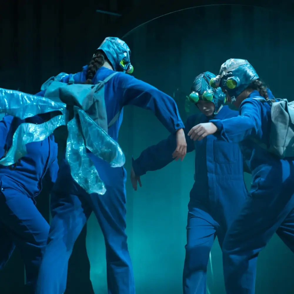 Young performers wearing blue insect costumes with wings and goggles during an IntoOpera stage production.