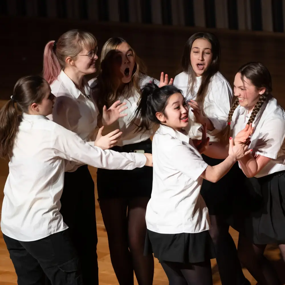 A group of secondary school students singing and acting together on stage during an IntoOpera performance.