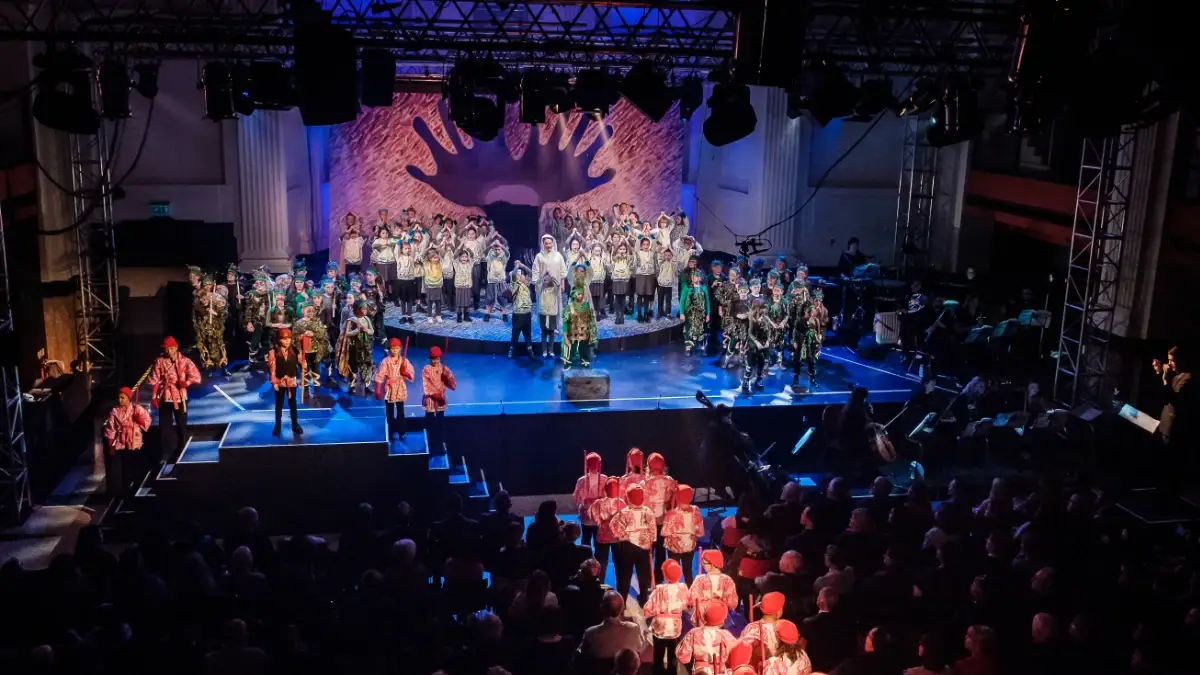 A large cast of children and young performers singing and performing together on stage during an IntoOpera production.