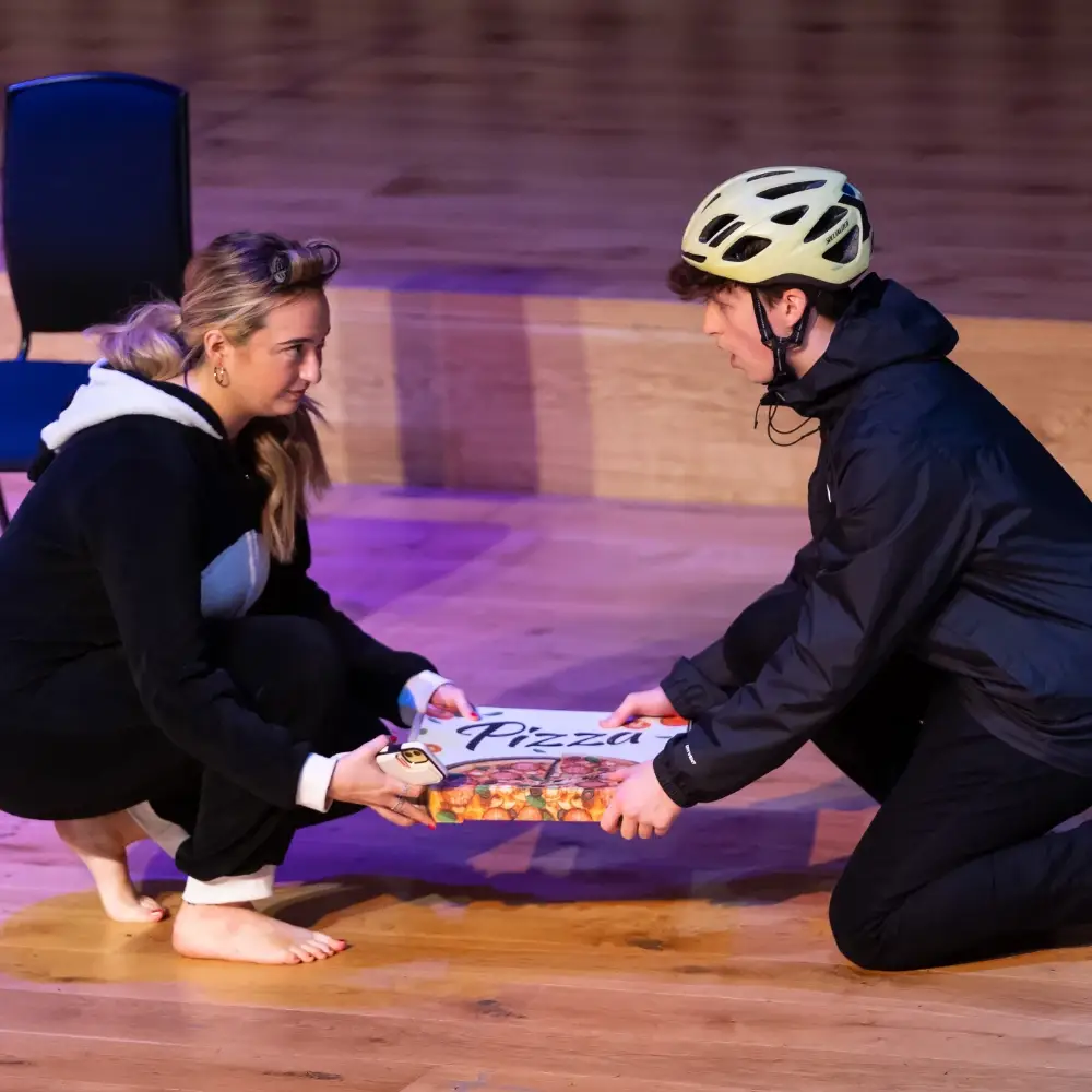 Two performers handling a pizza box during an opera performance
